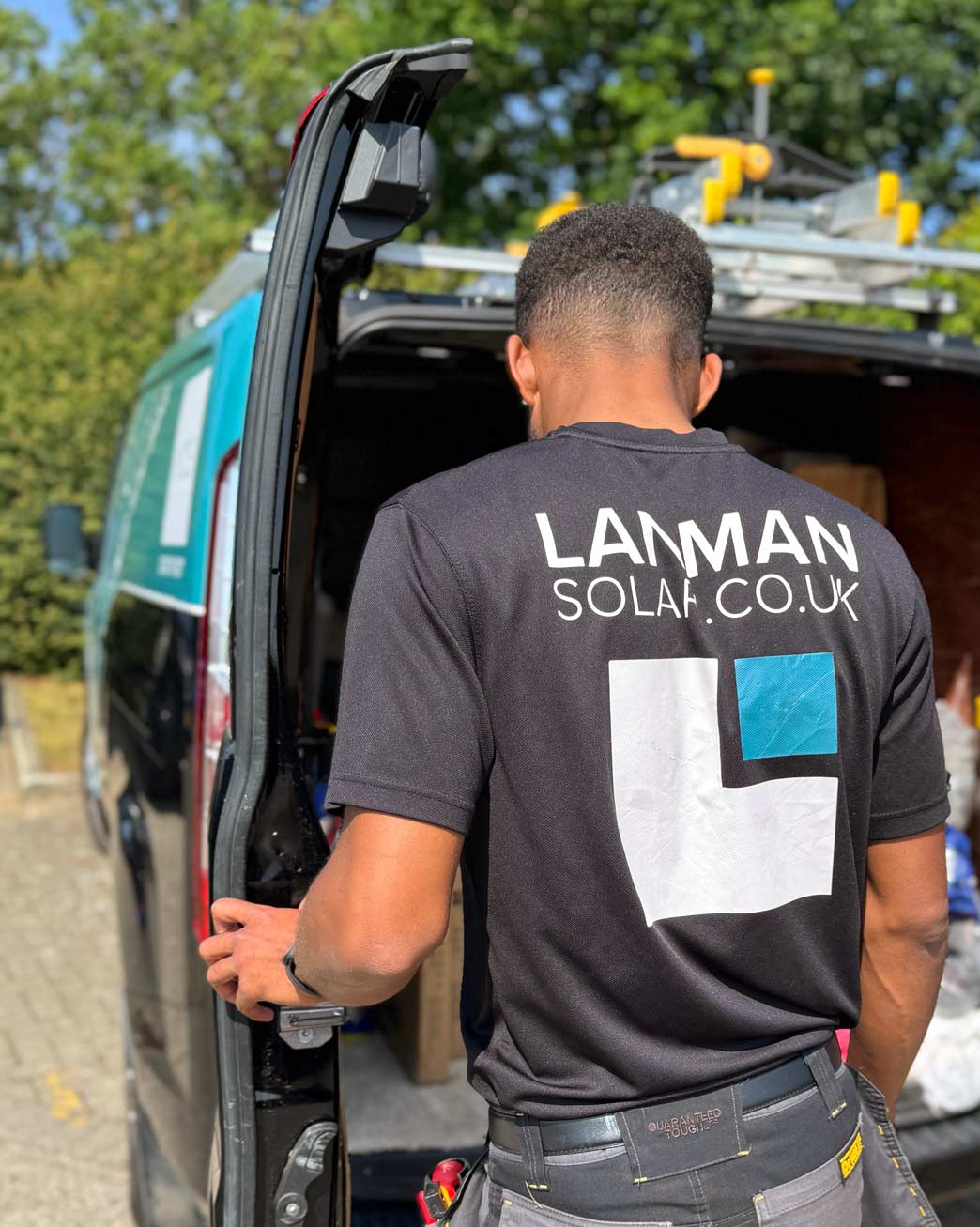 Grey pickup truck with Lanman Solar branding parked in front of a black house with solar panels installed on the roof under a blue sky.